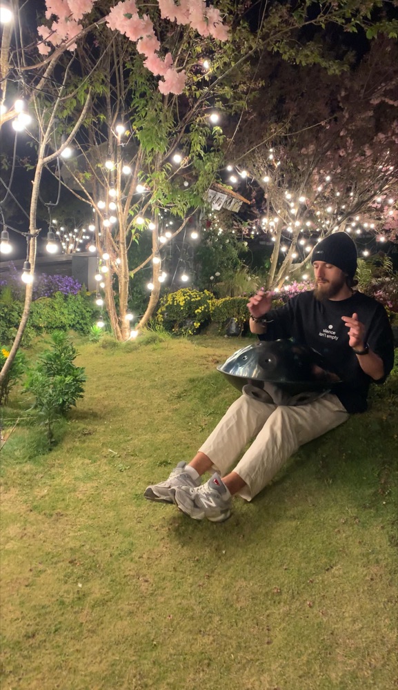 Nikita playing the handpan in a night garden strung with fairy lights.